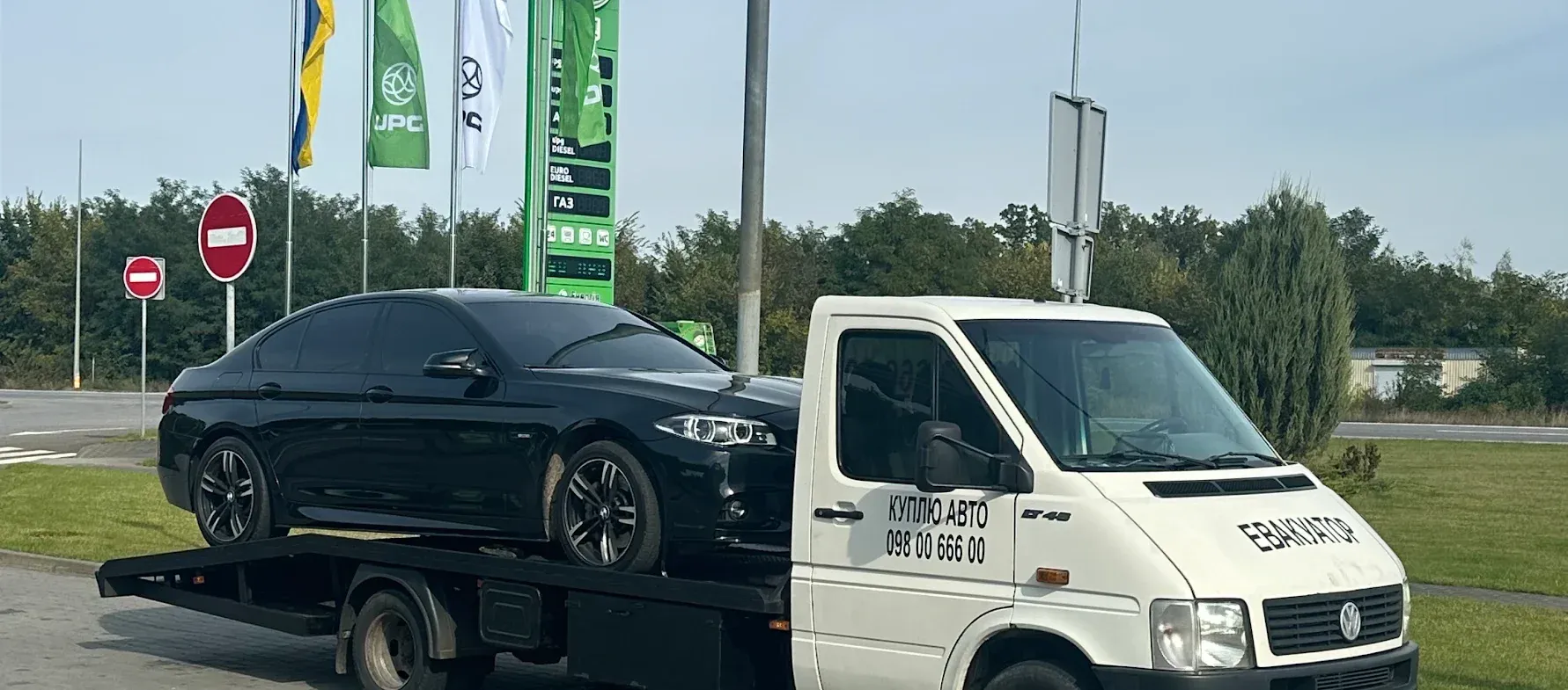 Седан BMW на платформі евакуатора біля заправки